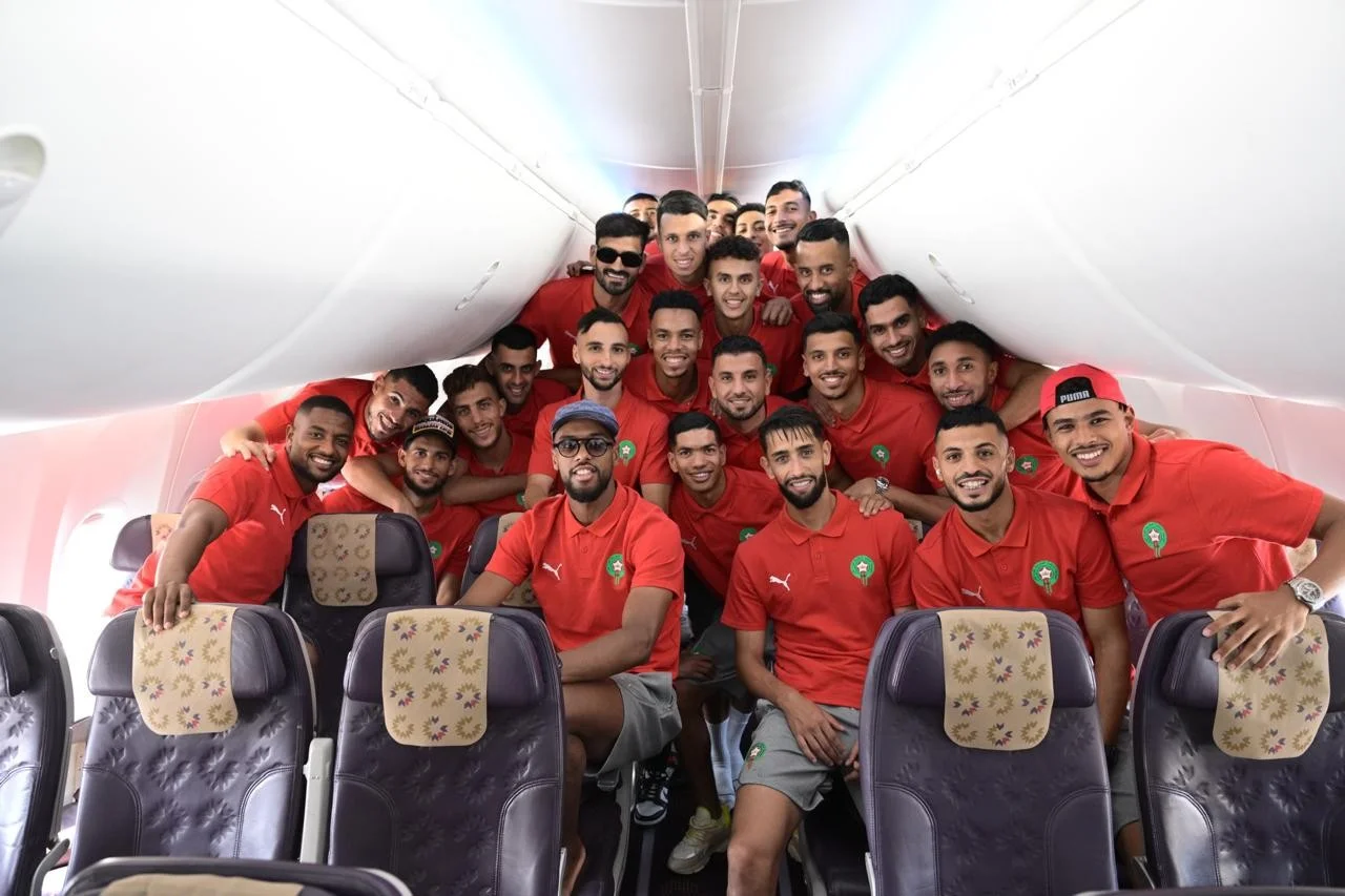 alt : Les joueurs de la sélection marocaine locale réunis à bord de l’avion les menant à Nairobi pour le CHAN 2024, sourire aux lèvres et tenues officielles aux couleurs nationales.