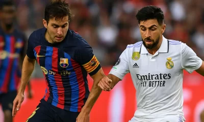 alt="Phase de jeu intense entre un joueur du FC Barcelone et un joueur du Real Madrid lors d’un match de LaLiga, avec le nouveau logo officiel de la compétition en arrière-plan"