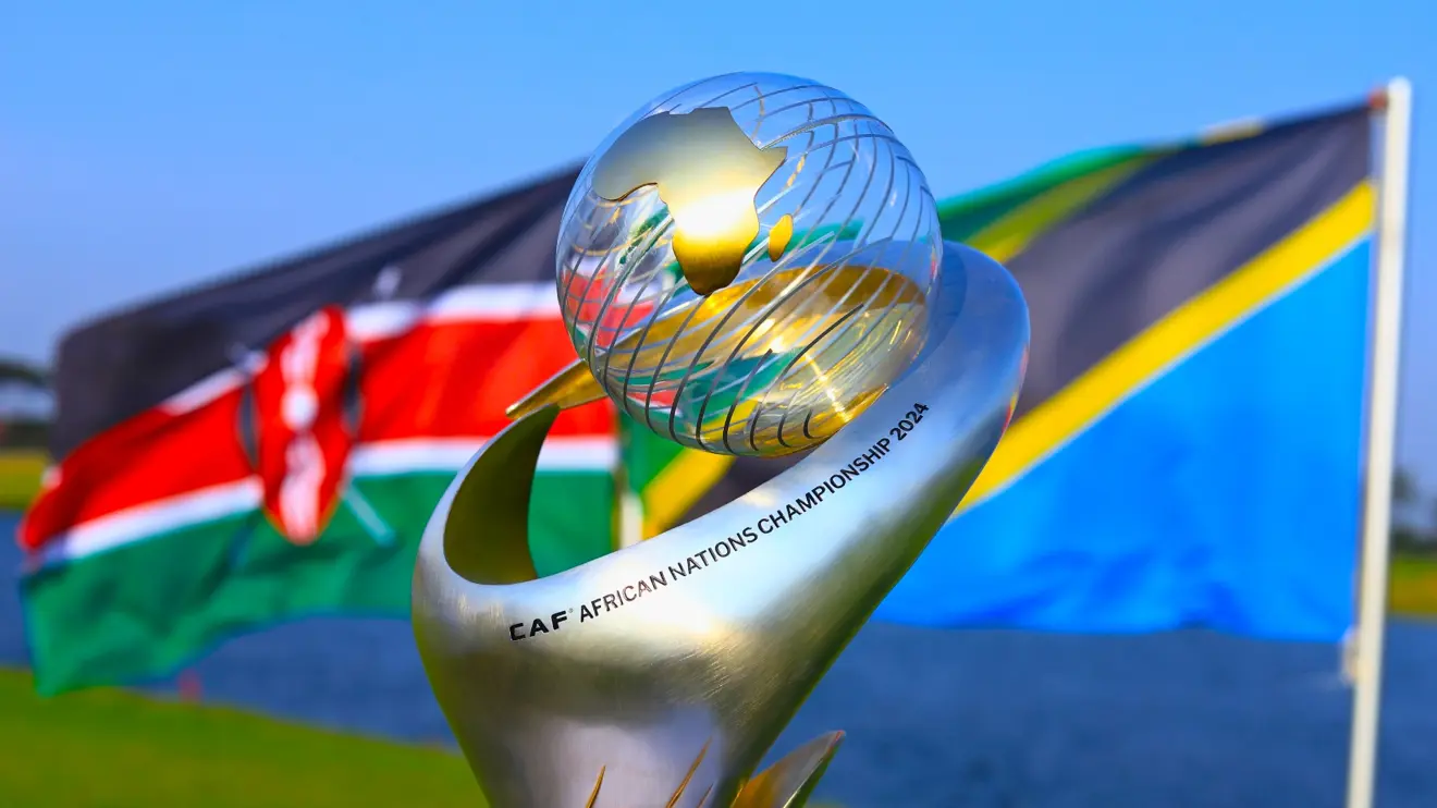 Le trophée du CHAN 2024 avec les drapeaux du Kenya et de la Tanzanie en arrière-plan, symboles de la co-organisation du tournoi.