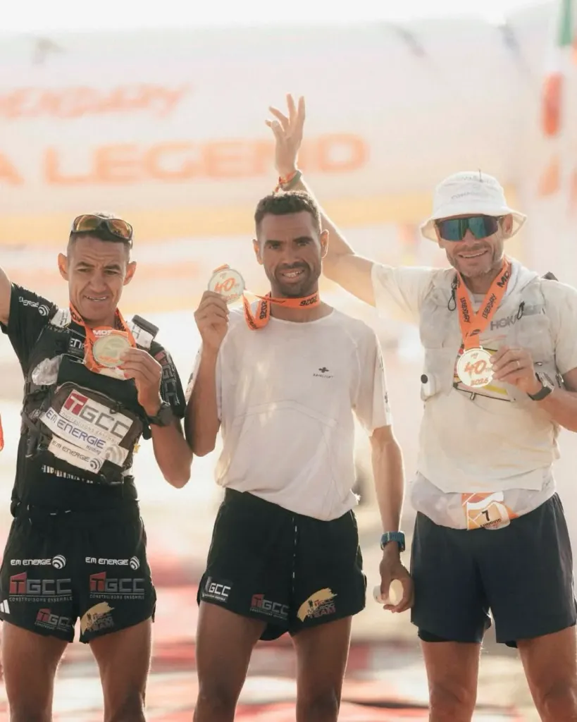 Alt= Le podium du marathon des Sables 2026 avec Mohamed El Mourabity, vainqueur de l'épreuve au milieu. A gauche son frère Rachid El Morabity, 2e, et le Français Ludovic Pommeret à droite.